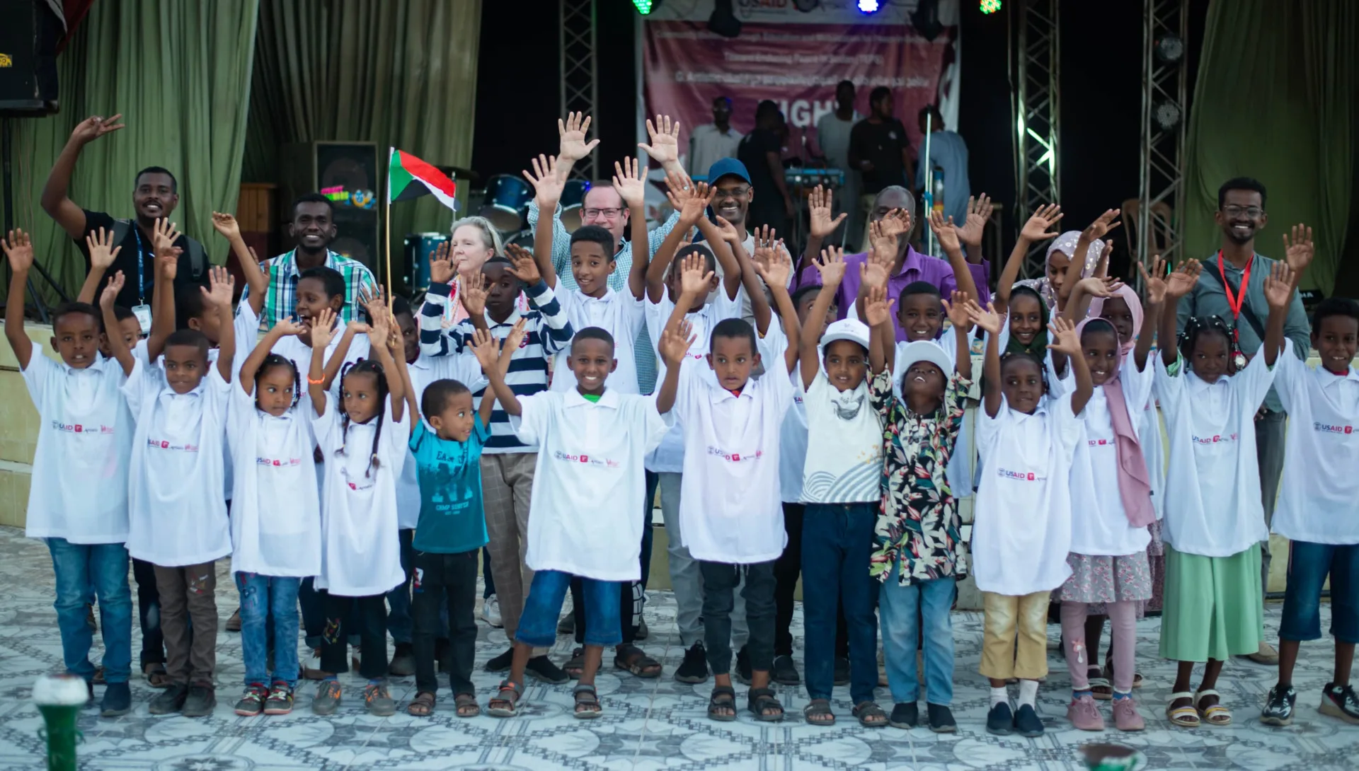 Children at a G.Artistic event with their hands raised together in the open air.