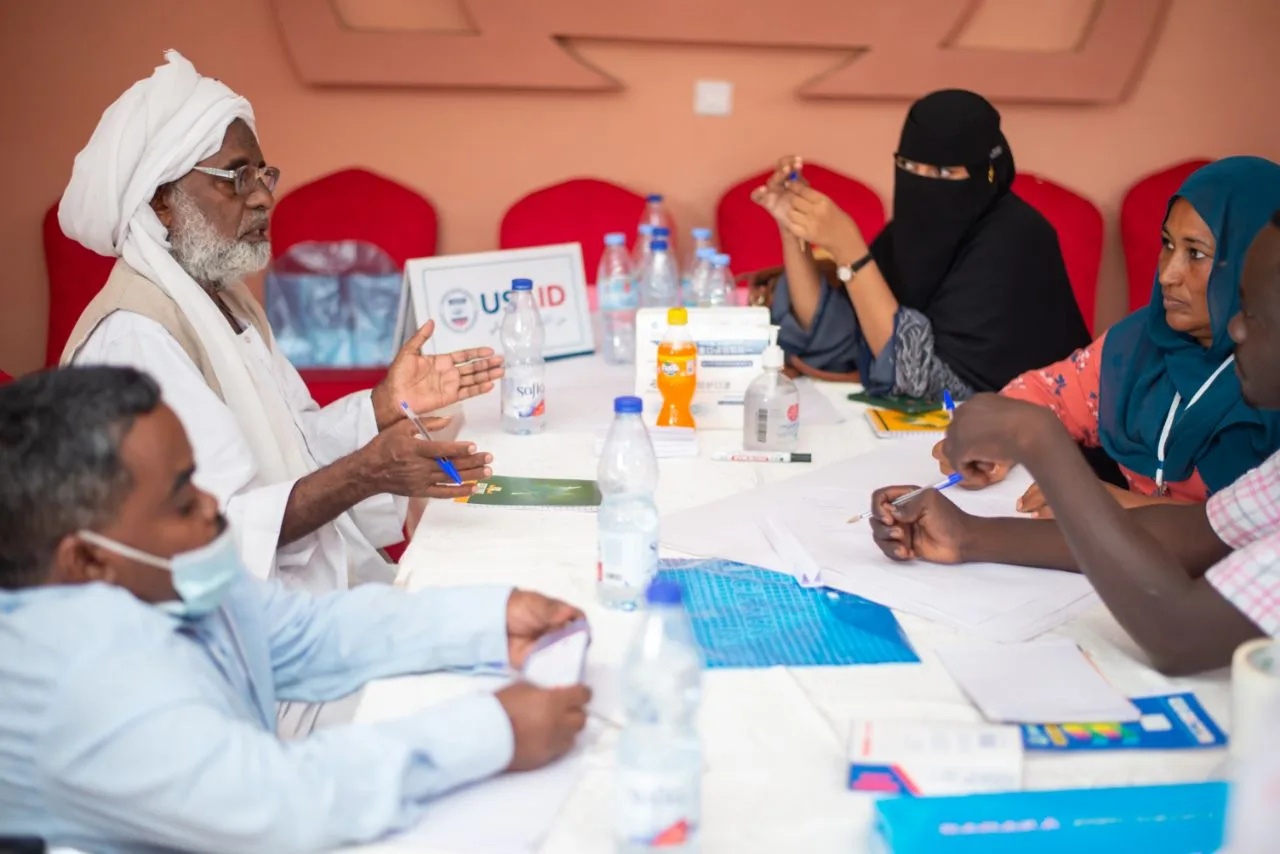 Community members and an elder in dialogue around a table