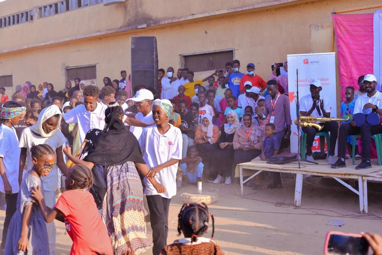 An open-air arts performance, a musician playing while young people dance.