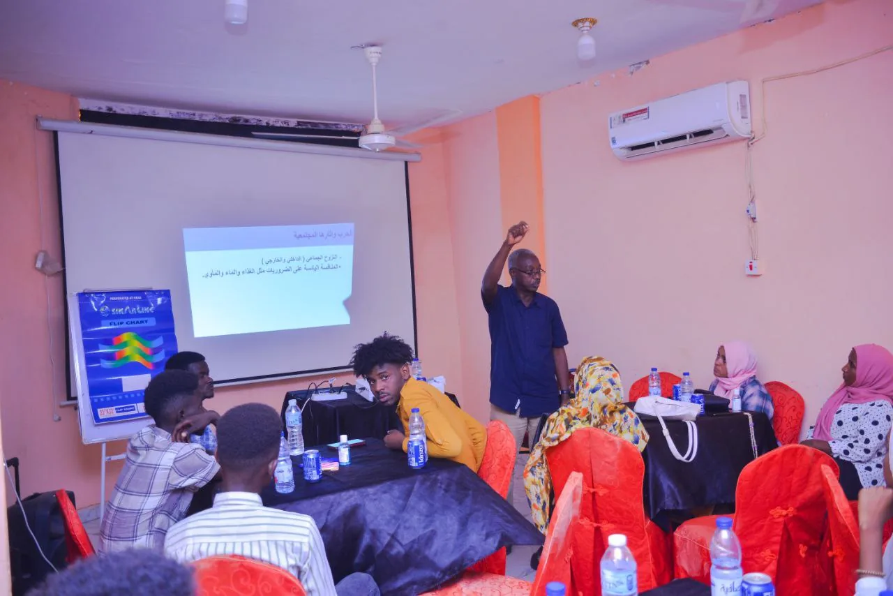 A community dialogue in progress, a facilitator standing before seated participants.